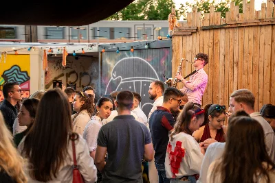 A summer courtyard party, the crowd turned towards Jovan Pastar playing saxophone on a small stage