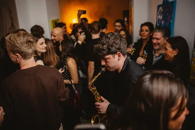 Jovan Pastar playing saxophone between the guests as a warm-lit room fills up