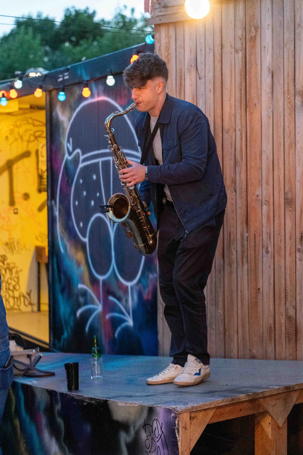 On a small open-air stage under string lights and street art