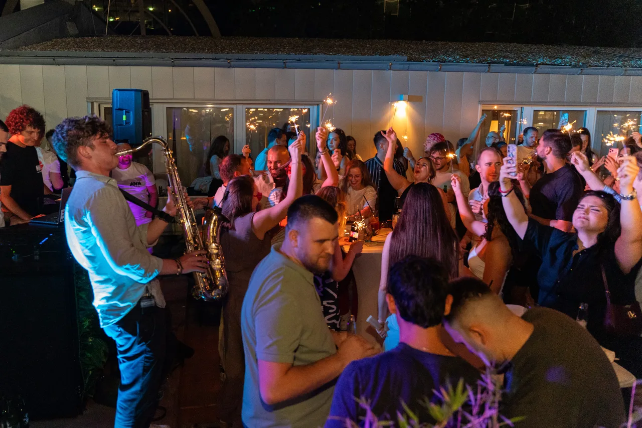 Sparklers lit over a night-time crowd as Jovan Pastar plays saxophone in blue light