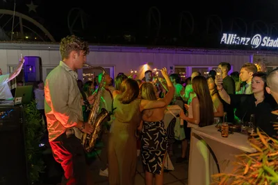 Jovan Pastar playing saxophone at a night party on a Vienna terrace, the crowd dancing behind him