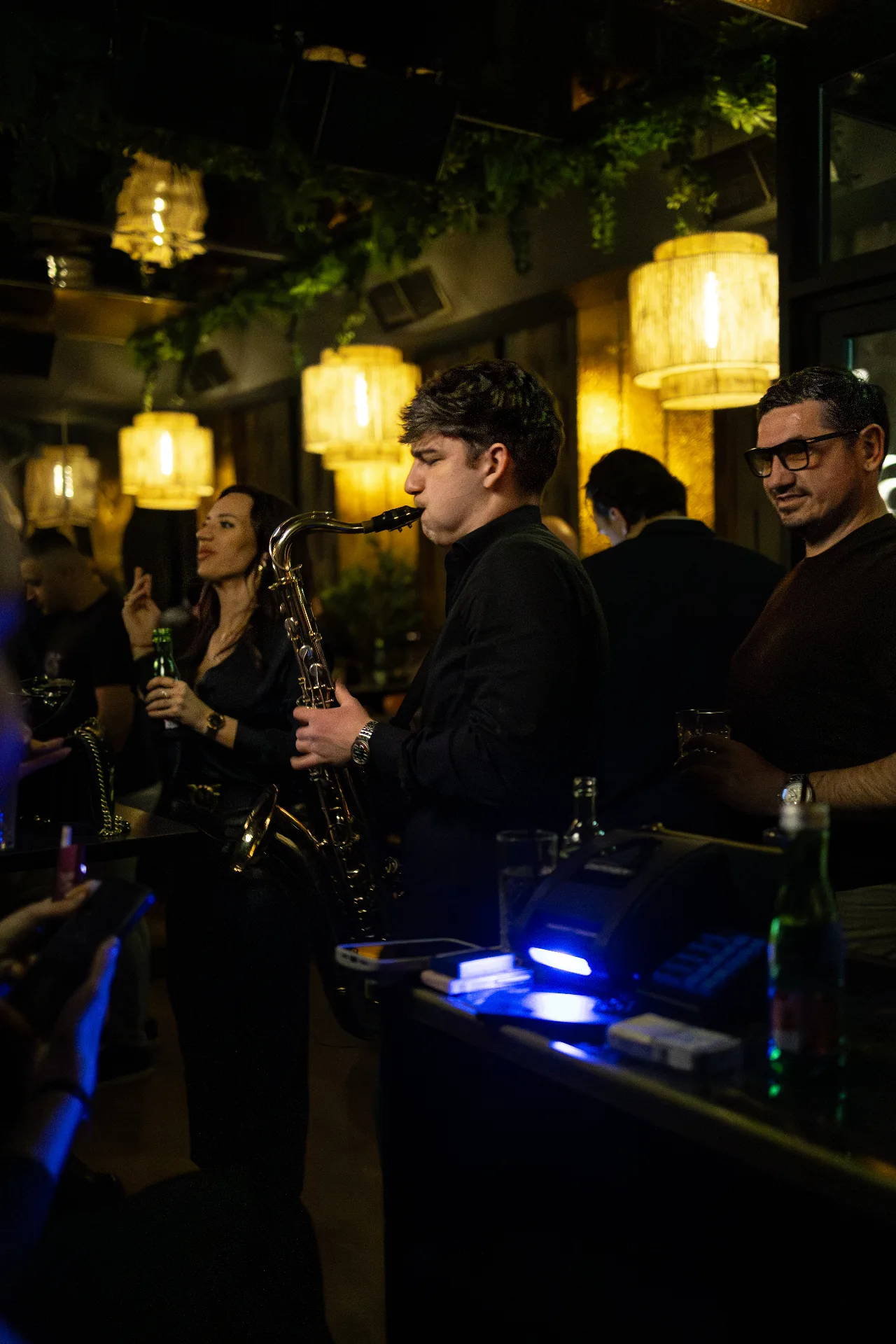 Jovan Pastar playing saxophone among the guests in a warm-lit venue