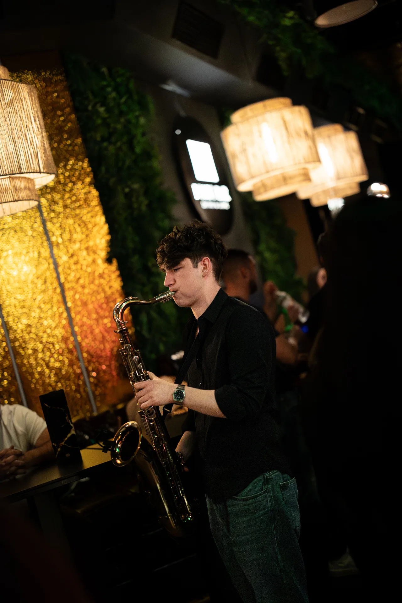 Jovan Pastar playing saxophone at a late set in a bar, a gold wall behind him