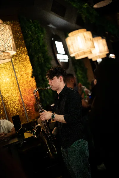 Jovan Pastar playing saxophone at a late set in a bar, a gold wall behind him